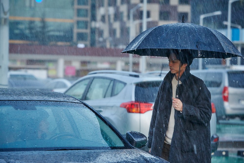 雨中撑伞的男人站在停放的汽车旁