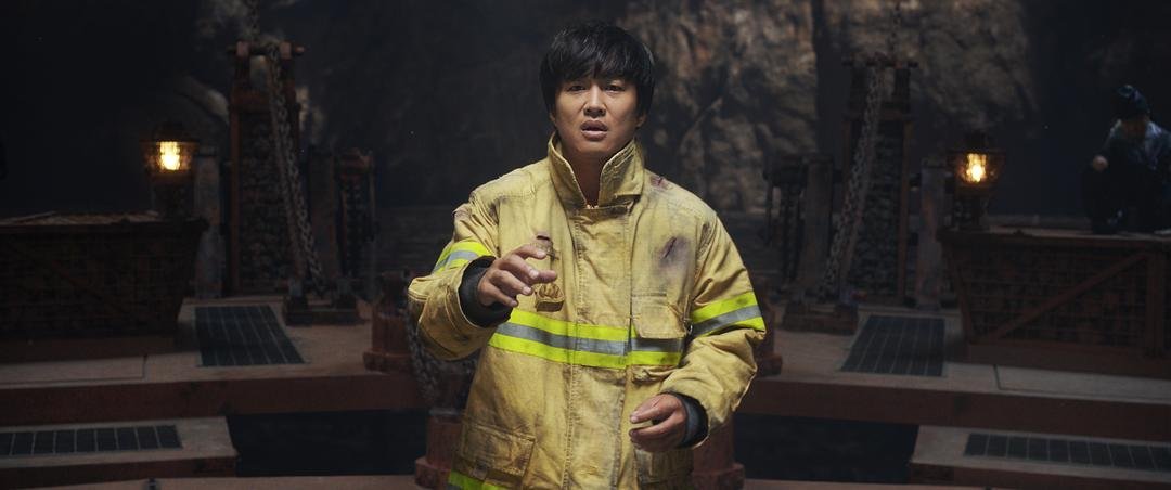 身穿黄色消防服的男子站在昏暗石殿中抬起一只手