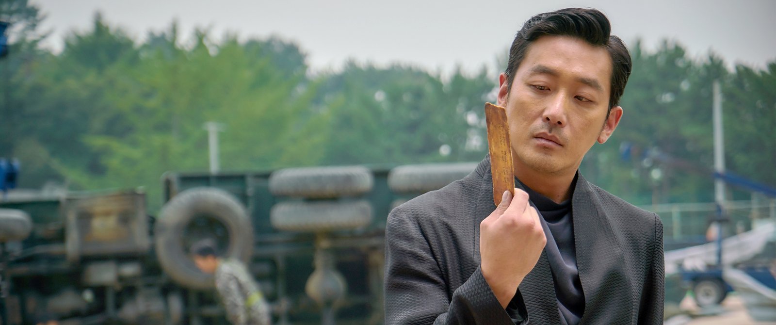 黑衣男子站在堆放轮胎的场地前，举着一件棕色长方形物品