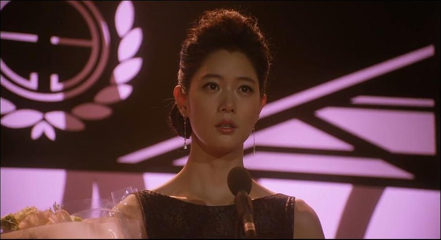 盘起头发的女子站在紫色灯光的舞台前面对麦克风