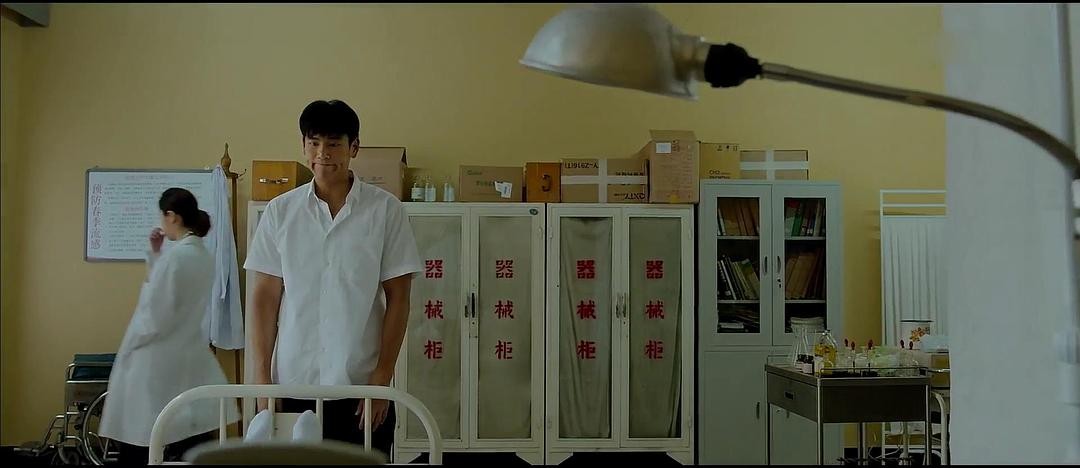 男子站在病床旁，身后的医护人员走过病房
