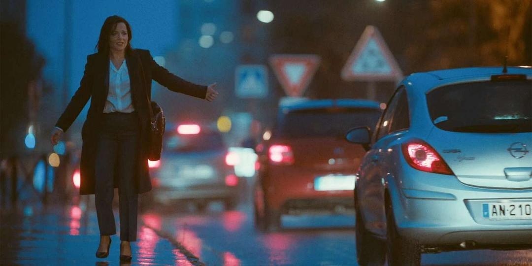 雨夜车流中一名穿深色西装的女子伸出手臂