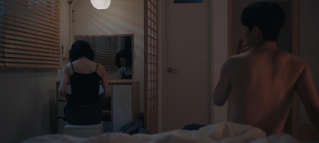 昏暗卧室里一名女子坐在梳妆台前，后方男子赤裸上身