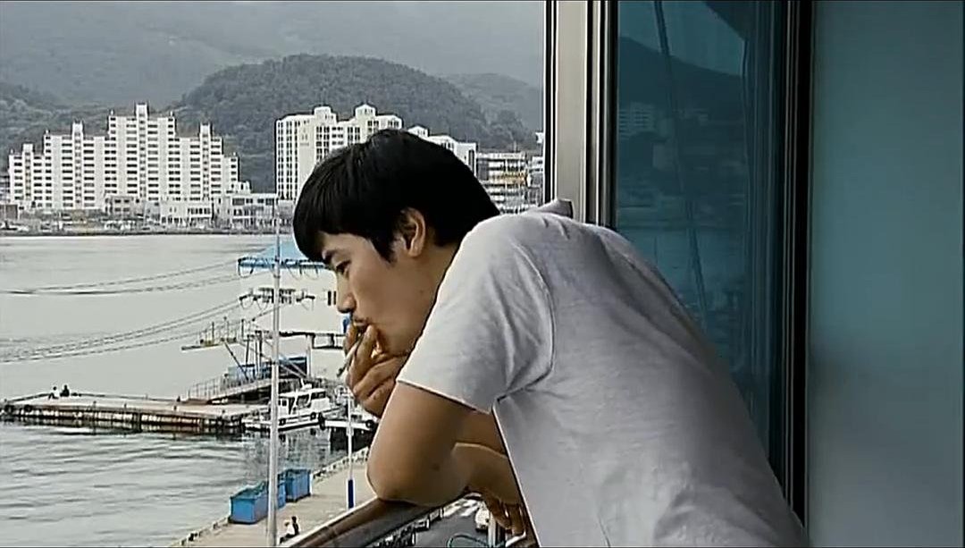 一名男子独自倚在窗边俯视港口