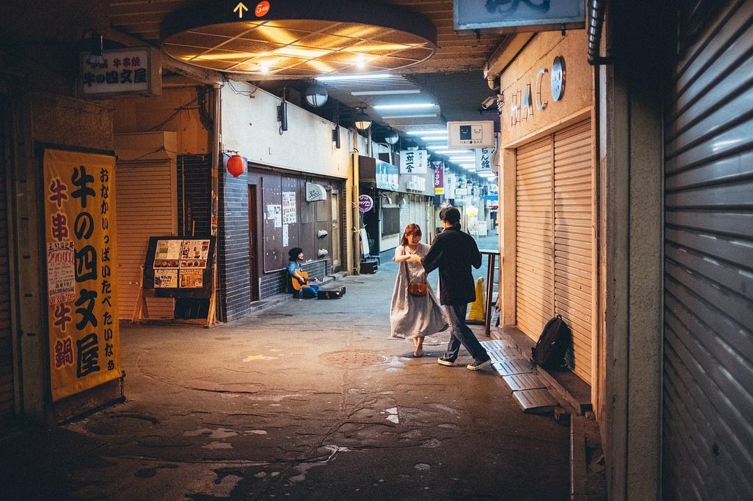 关闭卷帘门的商店街内,一男一女相对抬腿起舞