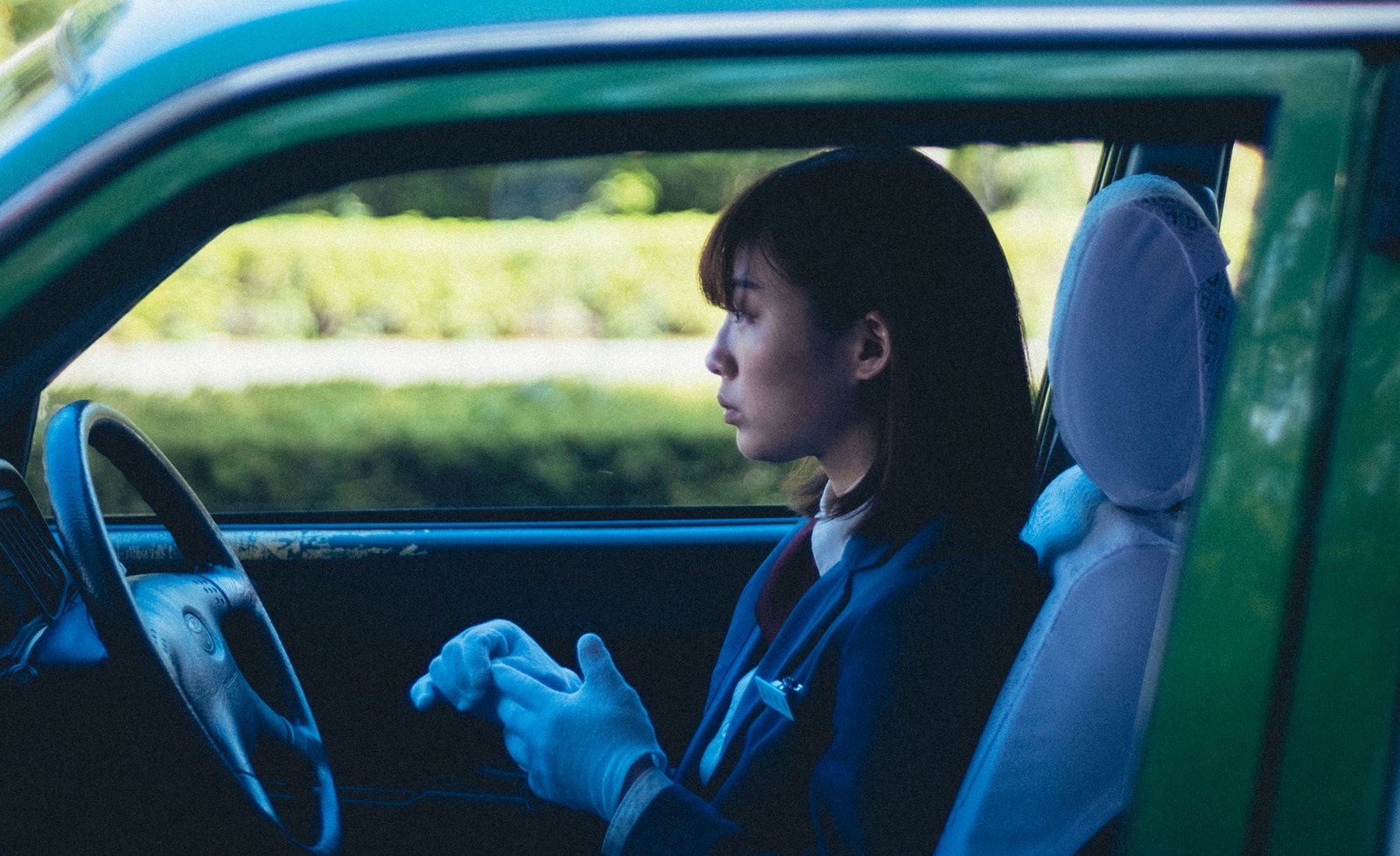 穿深色制服的女子坐在绿色出租车驾驶座,双手戴着浅色手套