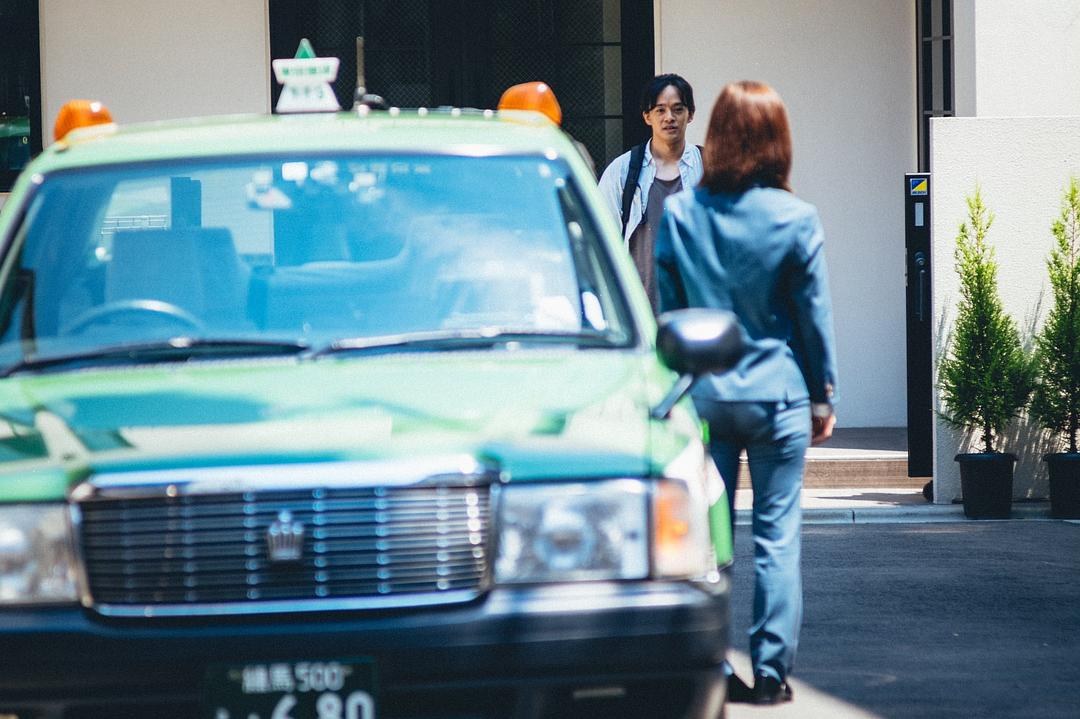 绿色出租车停在前景,一男一女在建筑入口处相对而立
