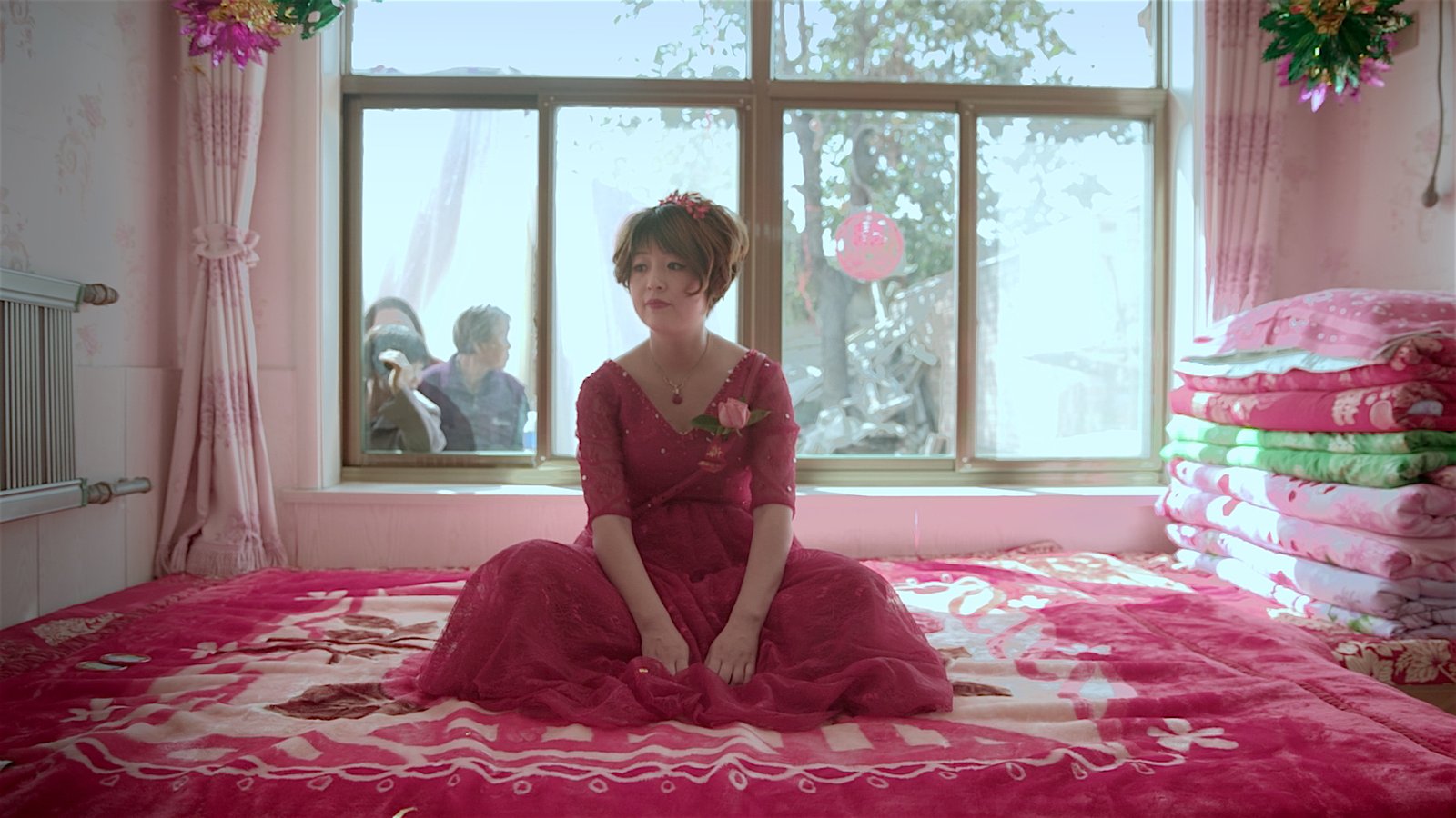 身穿红色礼服的短发女性坐在铺有红色床品的婚房里