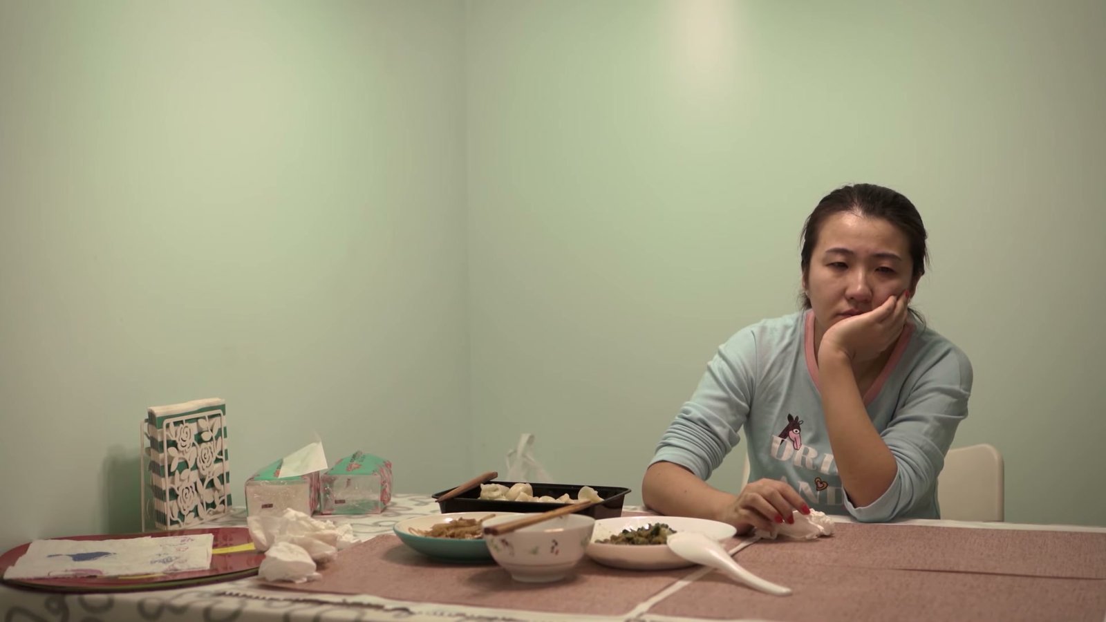 长发女性独自坐在餐桌边，手托着脸看向前方