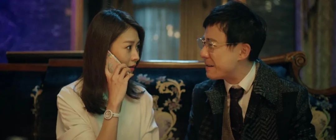 长发女子拿着手机与戴眼镜的男子并肩坐在沙发上