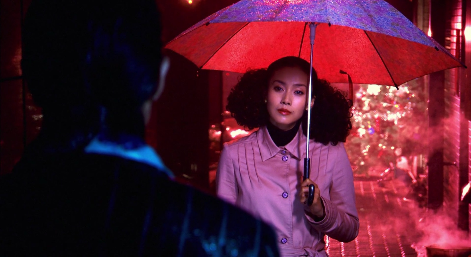 松子撑着红伞站在雨中,灯光映照出她的脸