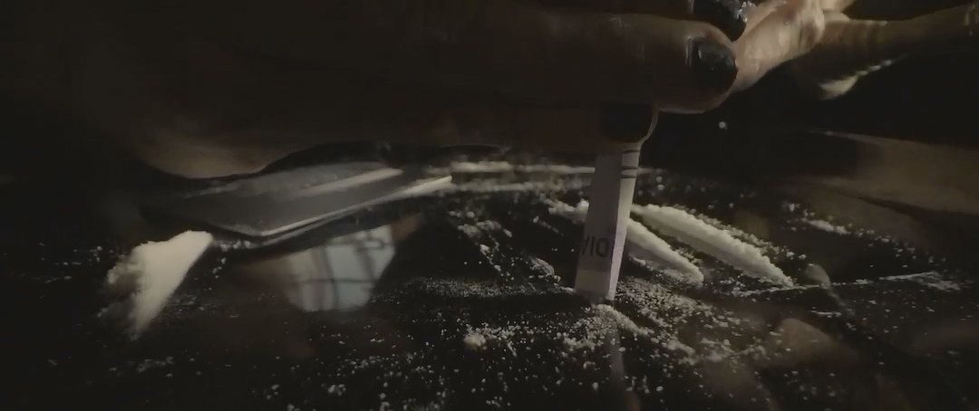 一只手用折起的钞票拨动桌面的白色粉末