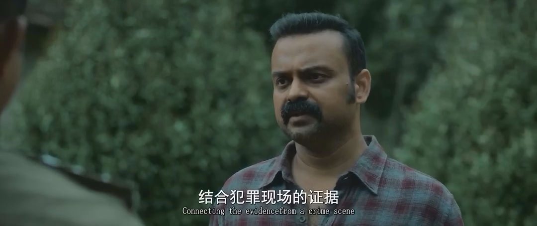 穿格纹衬衫的蓄须男子站在树林前说话