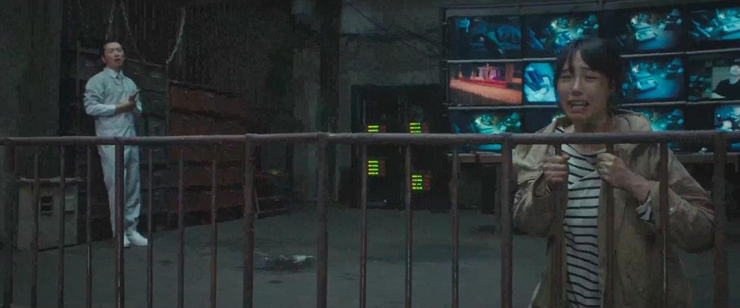 一名女子抓住金属围栏，身后站着一名男子和多块监控屏幕