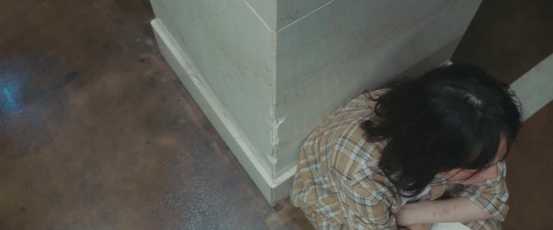 一名长发女子蜷缩在墙角地面上