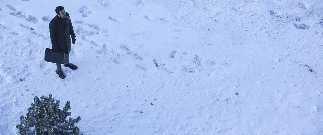 一名提着公文包的男子独自站在雪地里