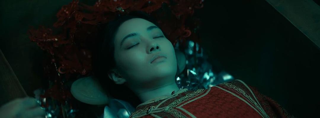 穿红色礼服的女子闭眼躺在棺中，头边围着红花