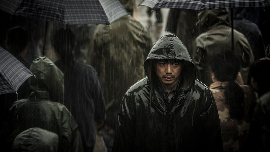 穿黑色连帽雨衣的男子低头穿过撑伞的人群