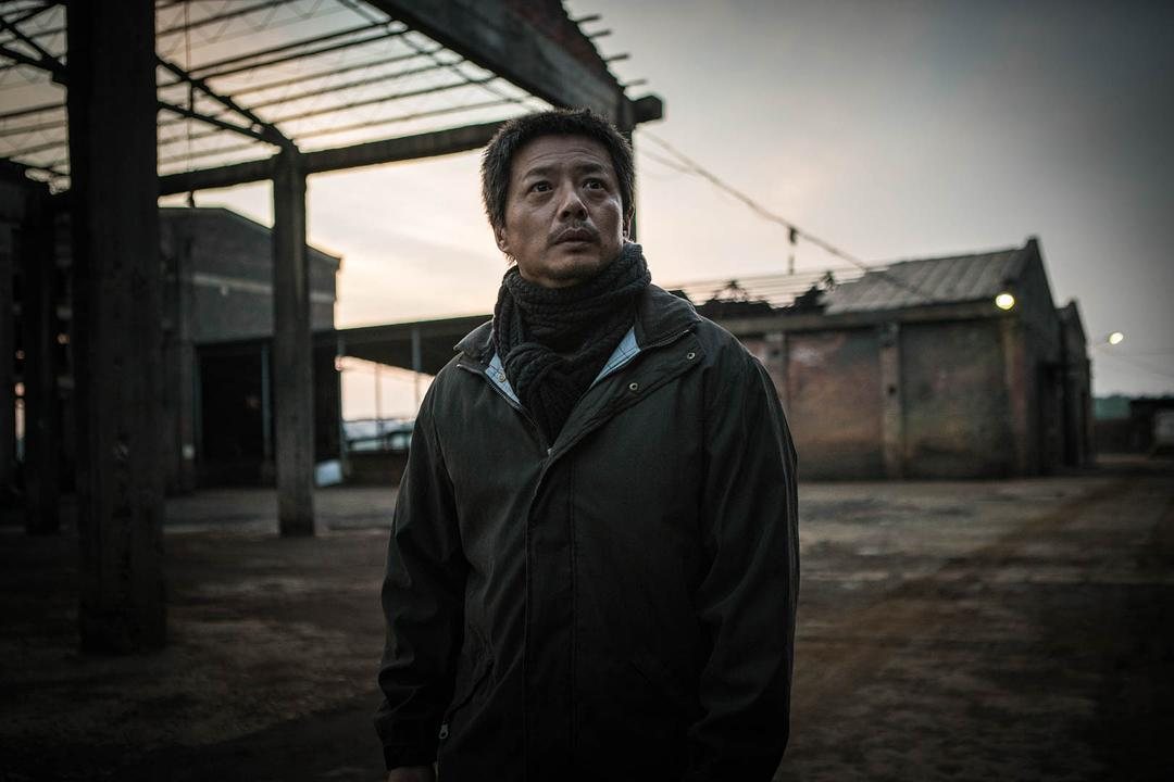 围着围巾的男子独自站在空旷厂区抬头望向上方