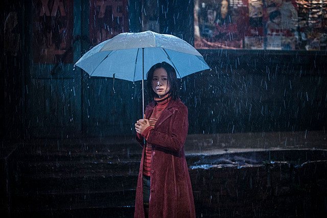 穿红色外套的女子撑着浅色雨伞站在夜雨中