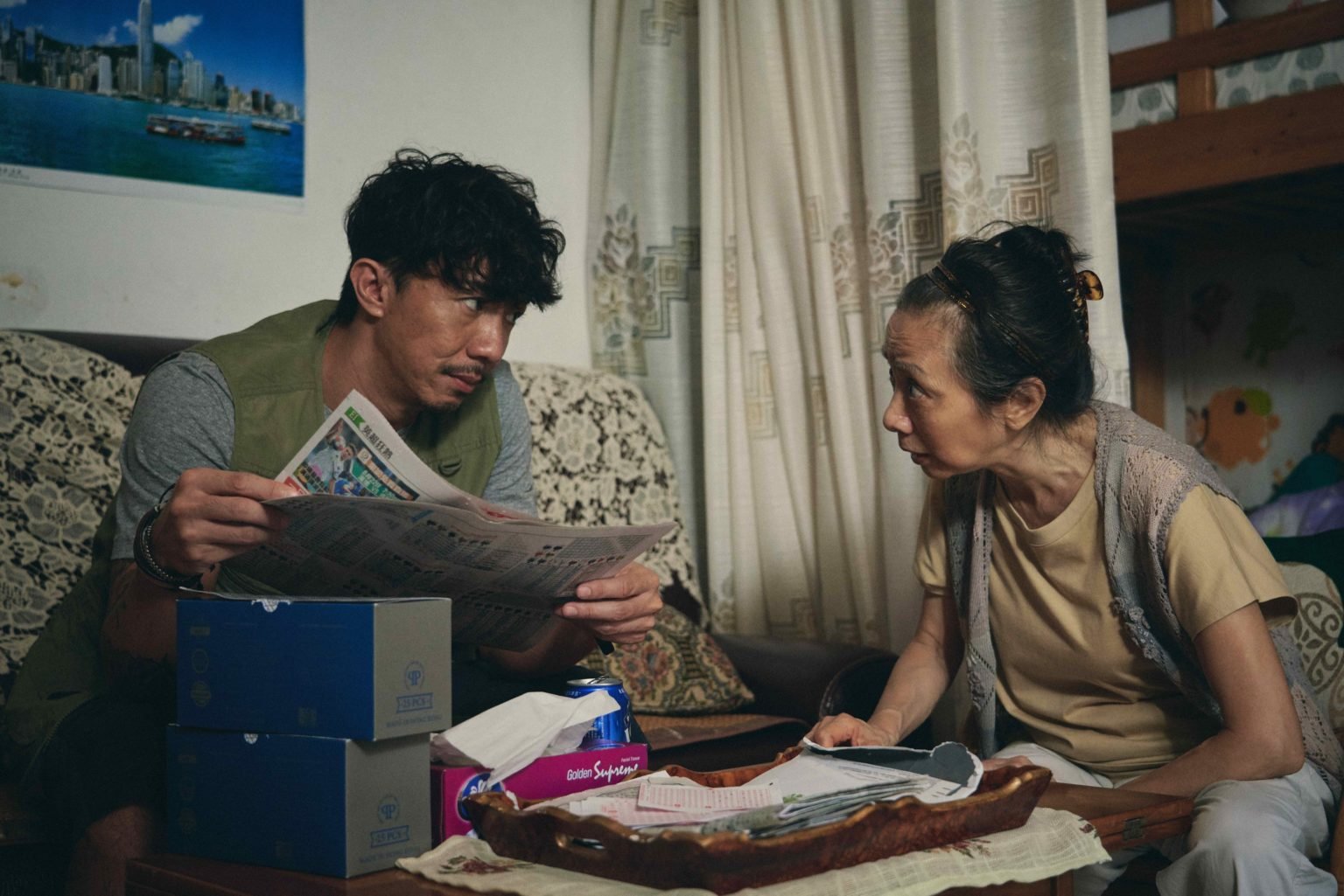 男子拿着报纸坐在沙发上，与旁边老妇交谈