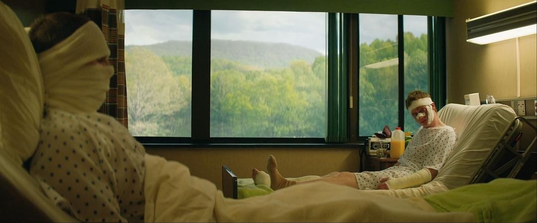 远处男子的头部和手臂缠着绷带，前景露出另一名病人的包扎头部