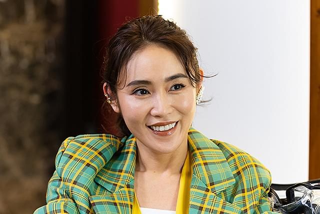一名穿黄绿色格纹外套的女子坐在桌前微笑