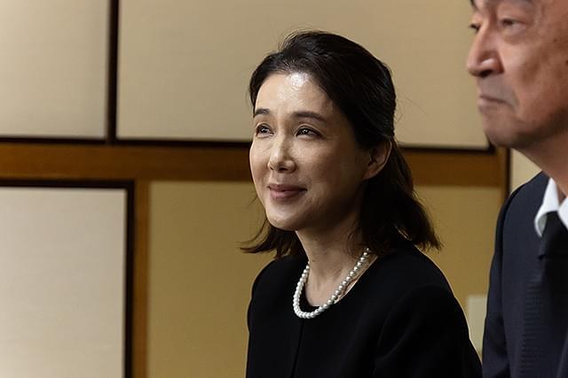 一名佩戴珍珠项链的女子与西装男子并肩站在室内