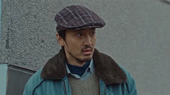 戴格纹鸭舌帽的男子站在灰色墙边