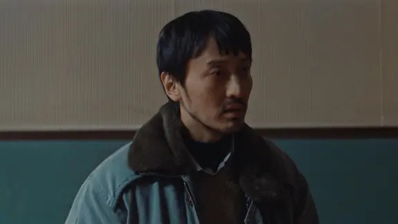穿翻领外套的男子在室内侧身看向一旁