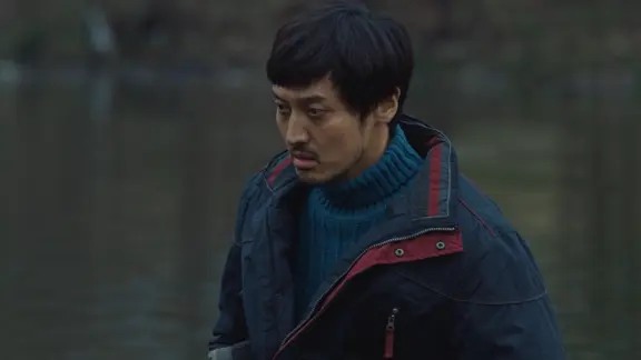 穿蓝色毛衣和深色外套的男子站在户外