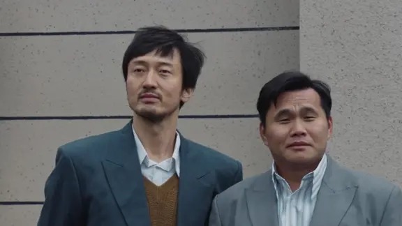 两名男子并肩站在灰色墙前