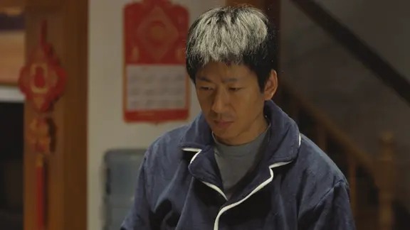 穿深色外套的男子低头站在室内
