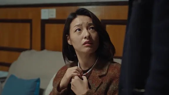 穿棕红外套的女子坐在室内仰头看向右侧
